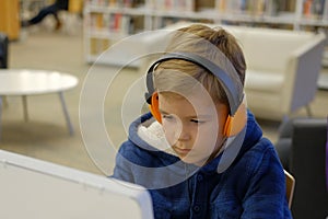 Elementary school boy sitting in library, using touchscreen computer for education