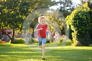 Elementary school child running on lawn in urban park on sunny day. Happy preteen boy having fun during walk. Outdoors activity