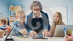 Elementary School Classroom: Enthusiastic Teacher Holding Tablet Computer Explains Lesson to Brill