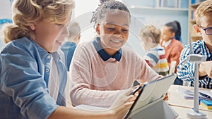 In the Elementary School: Girl and a Boy Work as a Team Using Tablet Computer. Diverse Classroom w