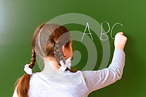 Elementary school girl stands in front of a blackboard and writes with chalk