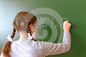 Elementary school girl stands in front of a blackboard and writes with chalk