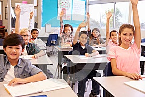 Elementary school kids in a classroom raising their hands photo