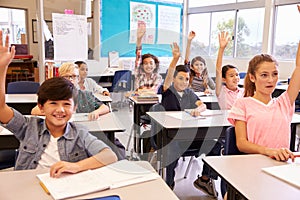 Elementary school kids in a classroom raising their hands photo
