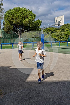 Elementary school kids having fun in school playground. Girl and boy wearing uniform running across field at break time