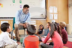 Elementary school kids sitting around teacher in a classroom