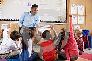 Elementary school kids sitting around teacher in a classroom