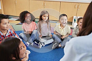 Elementary school kids sitting on floor looking at teacher