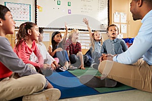 Elementary school kids and teacher sit cross legged on floor