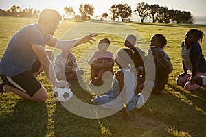 Elementary school kids and teacher sitting with ball in field