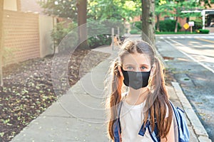 Elementary school student in a cloth dust mask with backpack in the street. Preteen girl is going to school in new