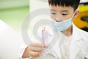 Elementary school student doing a science experiment. A boy looking at purple solution in a cylinder and feeling happy and fun on