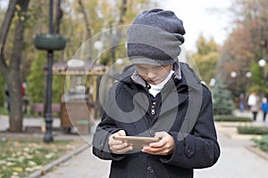 An elementary school student enthusiastically plays games on his smartphone, holding it in both hands. Entertainments of