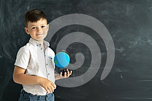 elementary school student standing with a globe near a chalk board in a classroom with a blackboard in the background