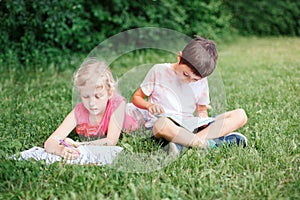 Elementary school students girl and boy doing homework outdoors. Children kids reading book and writing with pencil. Children
