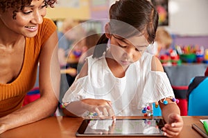 Elementary School Teacher And Female Pupil Drawing Using Digital Tablet In Classroom