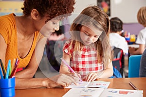 Elementary School Teacher Giving Female Pupil One To One Support In Classroom