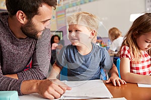 Elementary School Teacher Giving Male Pupil One To One Support In Classroom