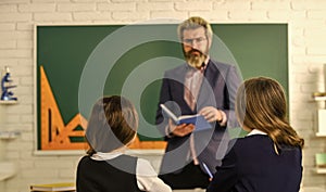 Elementary School Teacher Giving Support In Classroom. Pupil Wearing Uniform. Little Students Studying And Reading