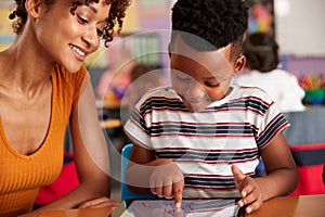 Elementary School Teacher And Male Pupil Drawing Using Digital Tablet In Classroom