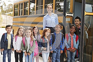 Elementary school teacher and pupils standing by school bus