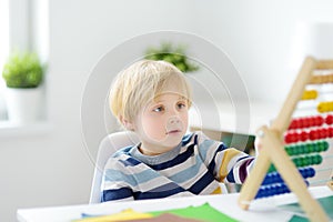 Elementary student boy doing homework at home. Child learning to count, solves arithmetic examples, doing exercises in workbook.