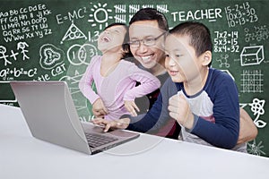 Elementary students using a laptop with their teacher