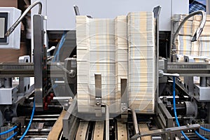 Elements of corton boxes are collected in stack. Conveyor line for the production of boxes. Machine cuts cardboard boxes from shee