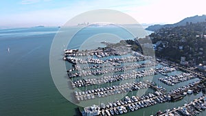 Elevated drone view of Sausalito\'s marina with San Francisco skyline and Bay Bridge in the far distance, on a clear day