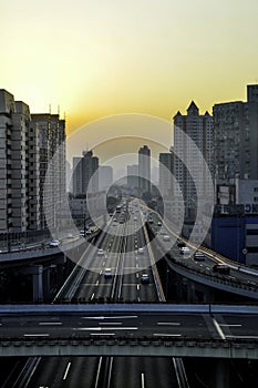 Elevated road in Shanghai. The sun sets on the horizon, the sky and the clouds / smog glow in warm orange tones. In the