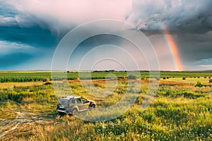 Elevated View Of Car SUV Parked Near Countryside Road In Summer Field Rural Landscape. Altered Rainy Sky With Rinbow photo