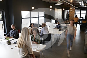 Elevated view of creative business colleagues working at desks and walking through a busy office