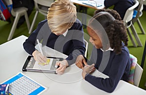 Elevated view of a girl and a boy using a tablet computer and stylus together in a primary school class