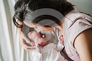 Elevated view of mother hugging cute newborn baby girl yawning at home. Family concept