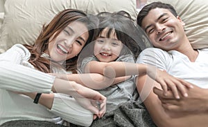 Elevated view portrait of happy family lying on bed and looking up and holding hands.