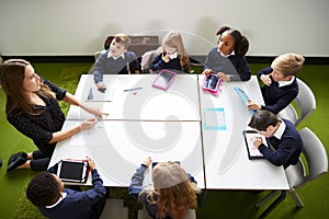 Elevated view of primary school kids sitting around a table in the classroom with their female teacher