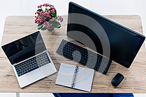 elevated view of table with flowers, empty textbook, laptop and computer