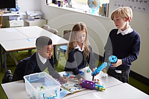 Elevated view of three primary school kids standing at a table in a classroom, working together with toy construction blocks