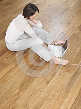 Elevated View Of Woman Using Laptop On Wood Flooring