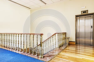 Elevator and stair area of a vintage building with hardwood floors and red marble steps