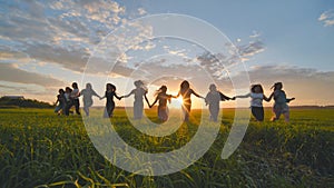 Eleven cheerful girls run to the meeting across the field in the summer, holding hands.