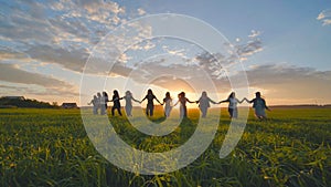 Eleven cheerful girls run to the meeting across the field in the summer, holding hands.