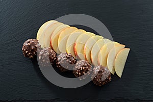 Eleven Peices of Sliced Apple and Five Nutty Chocolate Ice Cream Balls on a black Slated Serving Tray