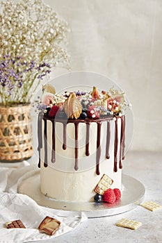 Elicious Boho Drip Cake with fruits and flowers on top on a white table