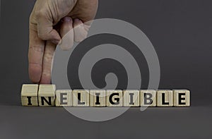 Eligible or ineligible symbol. Businessman turns wooden cubes and changes words Ineligible to Eligible. Beautiful grey table grey