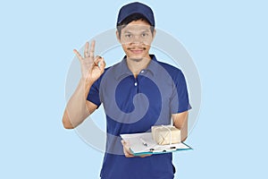 Elivery man holding box, clipboard and showing ok on blue background