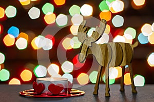 Elk wooden figurine and tea candle on background of colorful lights bokeh. Selective focus