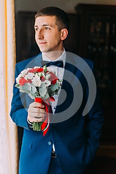 Ellegant bridegroom in blue suit with bow-tie holding a bouquet forward to meeting his bride