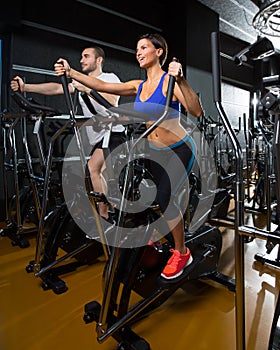 Elliptical walker trainer man and woman at black gym