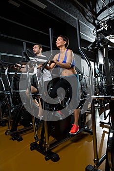 Elliptical walker trainer man and woman at black gym